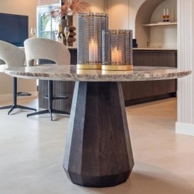 Modern round marble dining table with a white and brown veined top and dark mango wood faceted pedestal base, styled in a contemporary dining interior with decorative smoked glass lanterns.