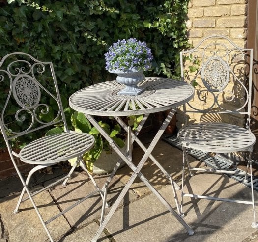 Outdoor garden furniture featuring a grey metal 2 seater bistro set with round table and two decorative chairs, styled on a garden patio.