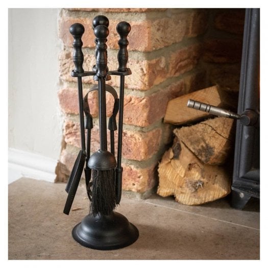 Fireplace accessories at Swanky Interiors featuring a traditional black metal companion set with poker, brush, shovel and tongs beside a wood-burning stove.