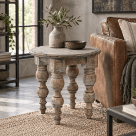 Rutland round rustic brown side table displayed beside a leather armchair in an industrial-style living room with black metal shelving, neutral decor and greenery.